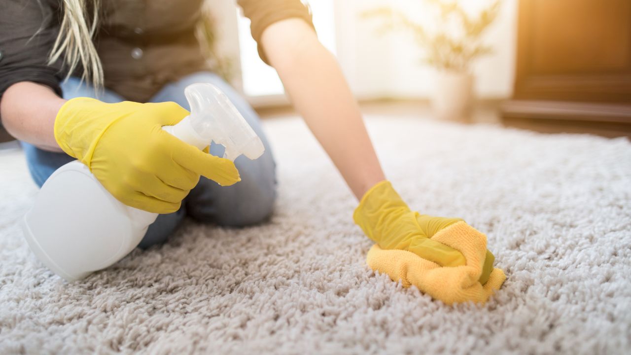 person spraying cleaning product on a carpet while wearing yellow gloves