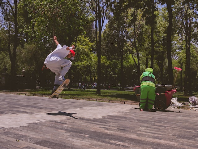 person skateboarding while someone cleans the park